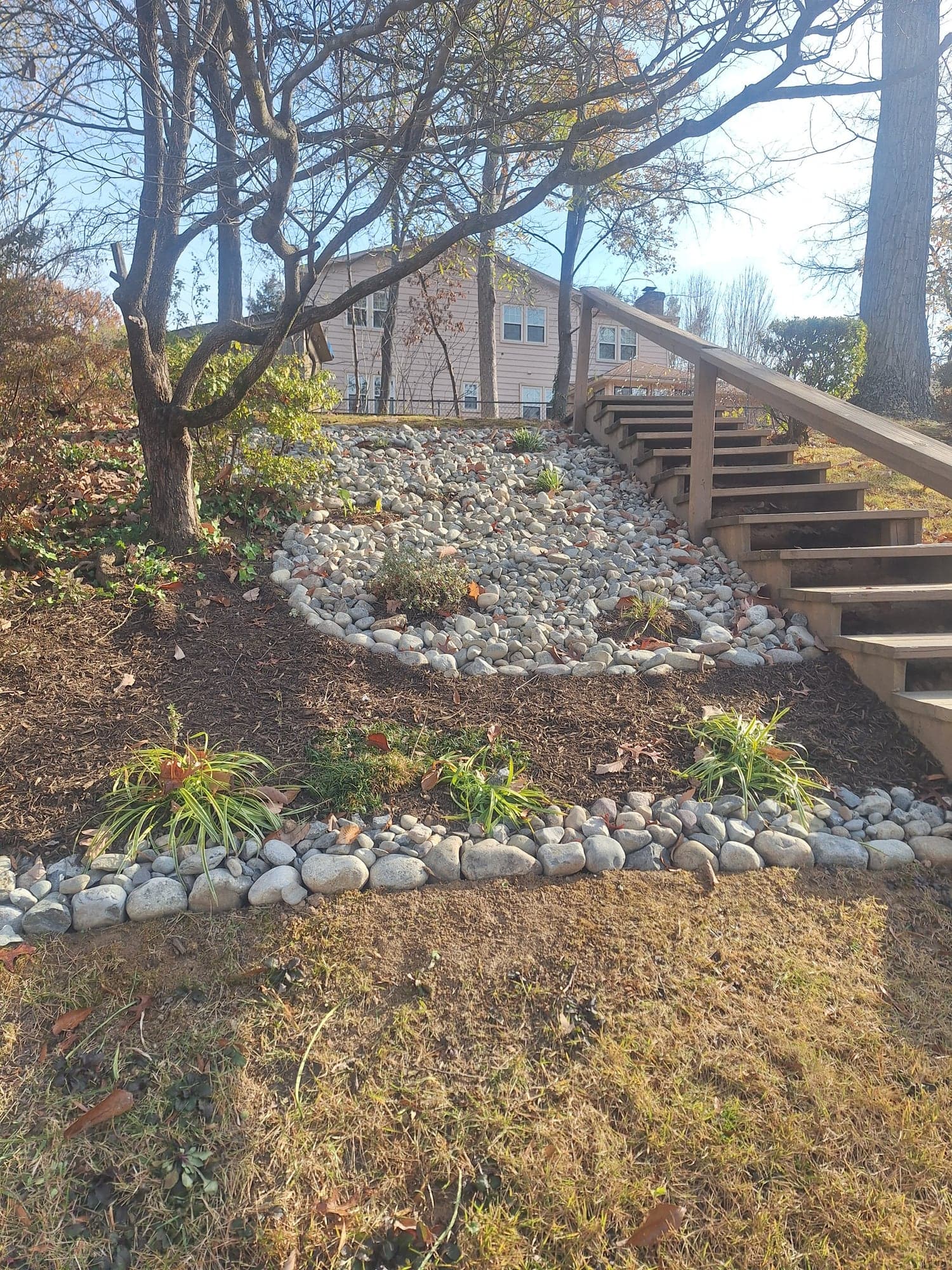 Mulched planting bed with a river-rock border and dry stream beside wooden outdoor stairs